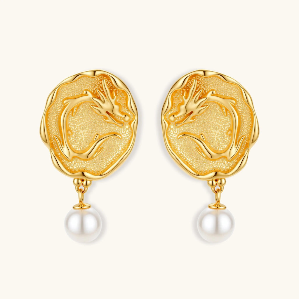 Ornate gold-plated dragon medallion earrings with white shell pearl drops on beige background, featuring detailed Chinese motifs.